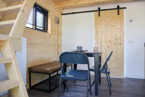 Helles Lodge-Innenraum mit Holzwänden, Esstisch, zwei Stühlen, Bank, Schiebetür und Treppe.