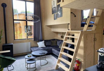 Gemütliches Tiny House mit Hochbett, Sitzecke, Holzverkleidung und großen Fenstern, minimalistisch gestaltet.