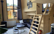Pequeña casa moderna con entrepiso, sofá gris, interior de madera y gran ventana en Bad Hoophuizen.