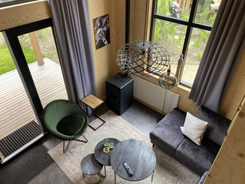 Wohnzimmer im Tiny House Bad Hoophuizen, Niederlande, modern eingerichtet mit Sessel, Sofa und großen Fenstern.