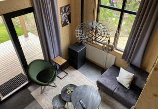 Wohnzimmer im Tiny House Bad Hoophuizen, Niederlande, modern eingerichtet mit Sessel, Sofa und großen Fenstern.