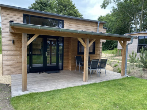 Kleines Holzhaus mit überdachter Terrasse und Gartenmöbeln, Tiny House at Bad Hoophuizen, Niederlande.