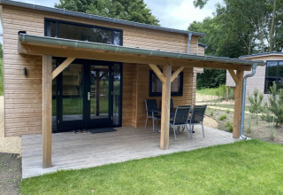 Kleines Holzhaus mit überdachter Terrasse und Gartenmöbeln, Tiny House at Bad Hoophuizen, Niederlande.