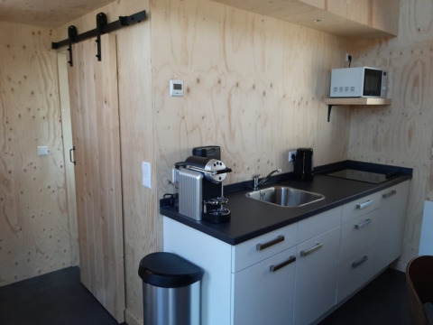 Moderne compacte keuken in Tiny House bij Bad Hoophuizen, Nederland, met houten wanden en witte kasten.