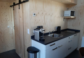 Moderne, kompakt køkken i Tiny House ved Bad Hoophuizen, Holland, med trævægge og hvide skabe.