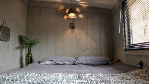 Chambre douillette au Tiny House de Bad Hoophuizen, Pays-Bas, avec literie grise et murs en bois.