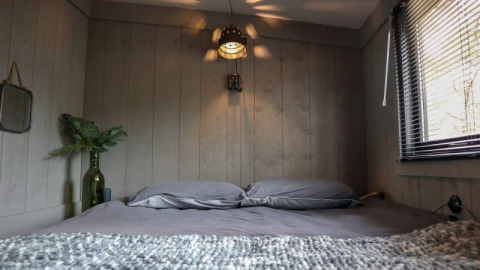 Gezellig slaapkamerinterieur in de Tiny House bij Bad Hoophuizen, Nederland, met grijs beddengoed en houten muren.