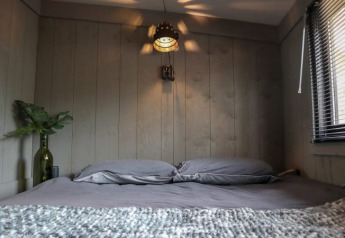 Knusse slaapkamer met grijs beddengoed in de Tiny House bij Bad Hoophuizen, Nederland, houten muren en raam.