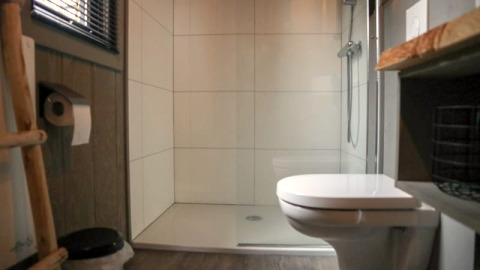 Salle de bain moderne avec toilettes, douche et sol en bois dans une Tiny House à Bad Hoophuizen, Pays-Bas.