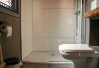 Salle de bain moderne avec toilettes, douche et sol en bois dans une Tiny House à Bad Hoophuizen, Pays-Bas.