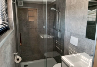 Salle de bain moderne et compacte avec douche en verre, toilettes et lavabo dans une tiny house à Bad Hoophuizen, Pays-Bas.