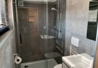 Kleines, modernes Badezimmer mit Glasdusche, Toilette und Waschbecken in einem Tiny House in Bad Hoophuizen, Niederlande.