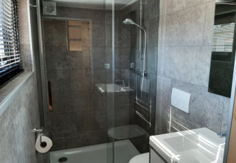 Moderne compacte badkamer met glazen douche, toilet en lavabo in een tiny house te Bad Hoophuizen, Nederland.
