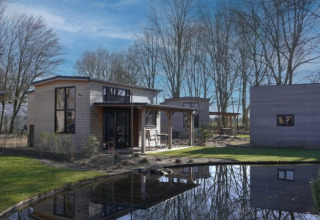 Tiny house moderna a Bad Hoophuizen nei Paesi Bassi, con stagno, alberi e cielo azzurro limpido.