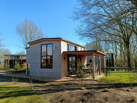 Foto eines modernen Tiny House mit Holzfassade und großen Fenstern in einer sonnigen, grünen Umgebung.