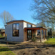 Billede af et moderne Tiny House med træfacade og store vinduer på en solrig dag omgivet af træer.