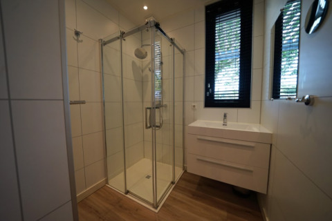 Moderne badkamer met glazen douche, wastafel en raam in het Modus XL verblijf in Bad Hoophuizen, Nederland.