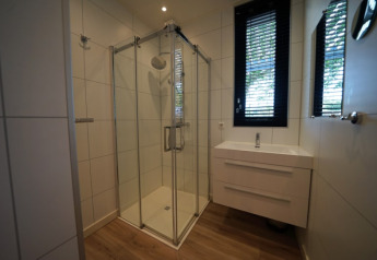 Moderne badkamer met glazen douche, wastafel en raam in het Modus XL verblijf in Bad Hoophuizen, Nederland.