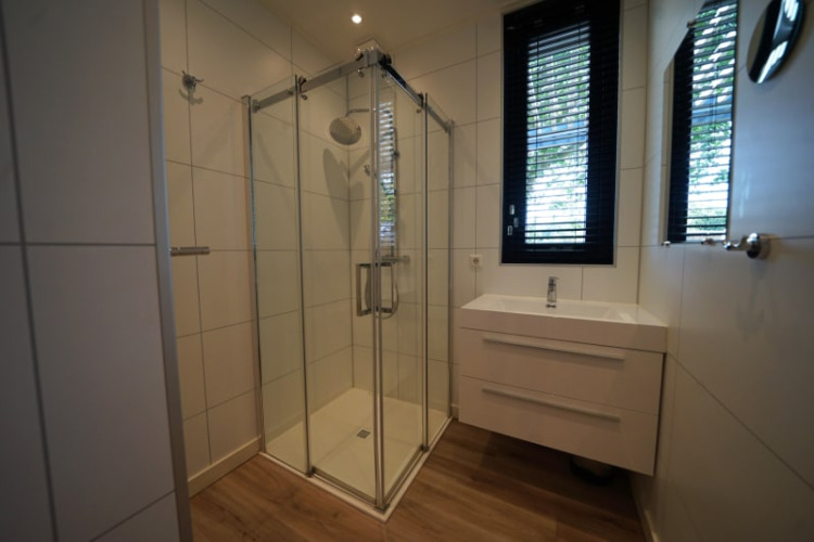 Baño moderno con ducha de cristal, lavabo y ventana en la cabaña Modus XL de Bad Hoophuizen, Países Bajos.