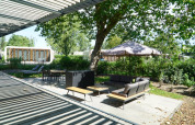 Zona de estar al aire libre con sofá, sombrilla y mesa de comedor en la cabaña Modus XL en Bad Hoophuizen.