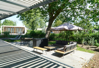 Zona relax all’aperto con divano, ombrellone e tavolo da pranzo al lodge Modus XL di Bad Hoophuizen, Olanda.