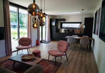 Soggiorno e cucina moderni nella lodge Modus XL a Bad Hoophuizen, Paesi Bassi, con grandi vetrate e arredi eleganti.
