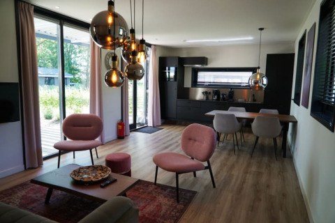 Salón moderno y cocina en la cabaña Modus XL en Bad Hoophuizen, Países Bajos, con ventanales y diseño elegante.