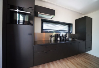 Moderne zwarte keuken in de Modus XL lodge in Bad Hoophuizen, Nederland, met toestellen en raam.