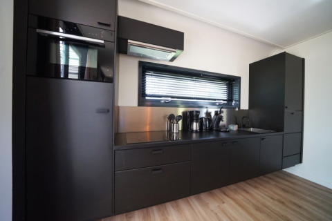 Moderne zwarte keuken in de Modus XL lodge in Bad Hoophuizen, Nederland, met toestellen en raam.
