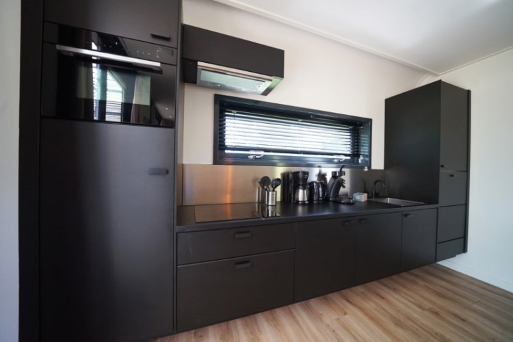 Cocina moderna negra en la cabaña Modus XL de Bad Hoophuizen, Países Bajos, con electrodomésticos y ventana.