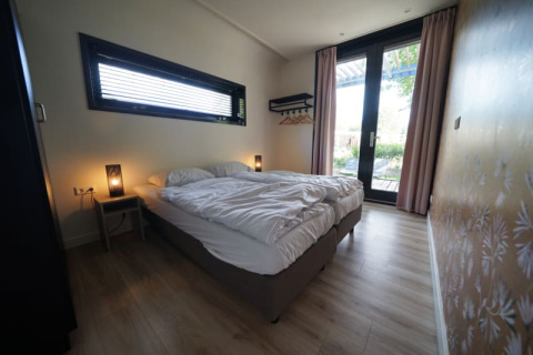 Camera da letto al Modus XL lodge di Bad Hoophuizen, Paesi Bassi, con letto matrimoniale e porte in vetro.