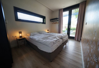 Dormitorio de la cabaña Modus XL en Bad Hoophuizen, Países Bajos, con cama doble y puerta de vidrio.