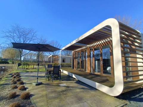 Moderne Modus-lodge met groot terras, tuinset en parasol in een zonnige, natuurlijke omgeving.