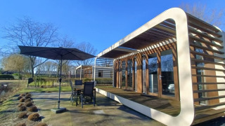 Moderne Modus-lodge met ruim terras, tuinmeubilair en parasol, gelegen in een zonnige, groene omgeving.