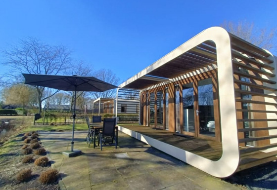 Moderne Modus-lodge met groot terras, tuinset en parasol in een zonnige, natuurlijke omgeving.