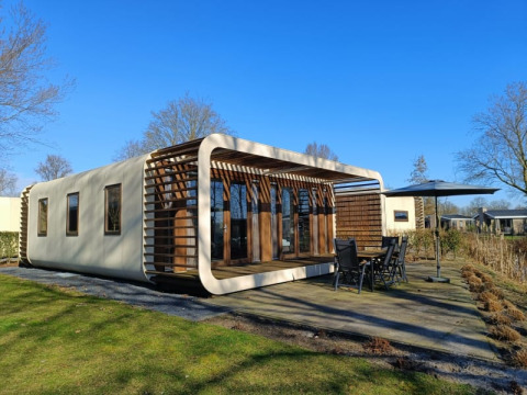 Moderne Modus-lodge bij Bad Hoophuizen in Nederland, met houten terras en tuinset onder blauwe lucht.