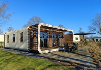 Moderne Modus-Lodge in Bad Hoophuizen, Niederlande, mit Holzterrasse und Gartenmöbeln bei klarem Himmel.