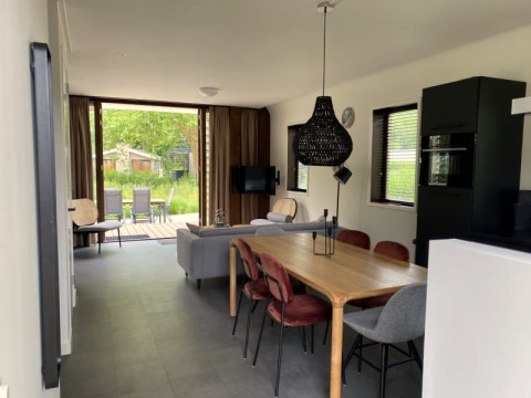 Intérieur moderne d’un lodge à Modus, Bad Hoophuizen, Pays-Bas, avec salle à manger, canapé et vue jardin.