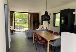 Intérieur moderne d’un lodge à Modus, Bad Hoophuizen, Pays-Bas, avec salle à manger, canapé et vue jardin.