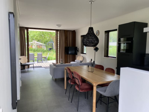 Interni moderni di una lodge a Modus, Bad Hoophuizen, Paesi Bassi, con sala da pranzo, divano e vista sul giardino.