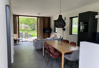 Modern lodge interior at Modus in Bad Hoophuizen, Netherlands, with dining area, sofa, and garden view.