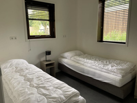 Chambre lumineuse avec deux lits simples, draps blancs, table de chevet et fenêtres à Modus, Bad Hoophuizen, Pays-Bas.