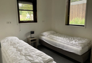 Chambre lumineuse avec deux lits simples, draps blancs, table de chevet et fenêtres à Modus, Bad Hoophuizen, Pays-Bas.
