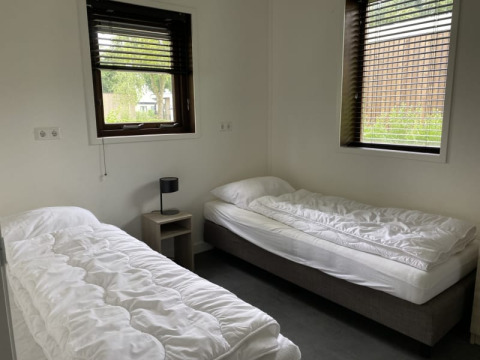 Habitación luminosa con dos camas individuales, ropa de cama blanca y ventanas en Modus, Bad Hoophuizen, Países Bajos.
