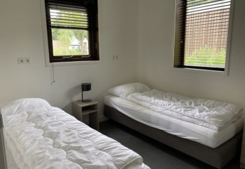 Helles Zimmer mit zwei Einzelbetten, weißer Bettwäsche, Nachttisch und Fenstern im Modus, Bad Hoophuizen.