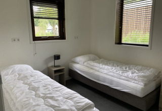 Habitación luminosa con dos camas individuales, ropa de cama blanca y ventanas en Modus, Bad Hoophuizen, Países Bajos.