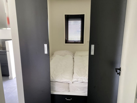 Petite chambre avec un lit, des couettes blanches et des portes coulissantes à Modus lodge à Bad Hoophuizen.