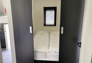 Petite chambre avec un lit, des couettes blanches et des portes coulissantes à Modus lodge à Bad Hoophuizen.