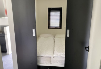 Piccola camera da letto con letto, piumoni bianchi e porte scorrevoli presso il lodge Modus a Bad Hoophuizen.