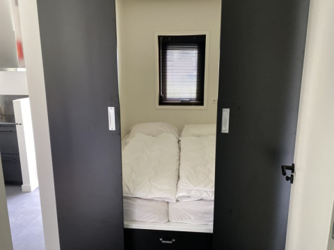 Kleine slaapkamer met bed, witte dekbedden en schuifdeuren in Modus lodge te Bad Hoophuizen, Nederland.